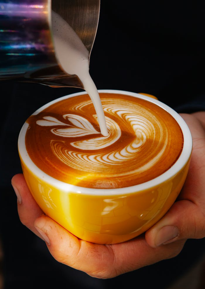 Unrecognizable professional male barista with mug of coffee making latte art with leaf pattern in modern coffee house during work